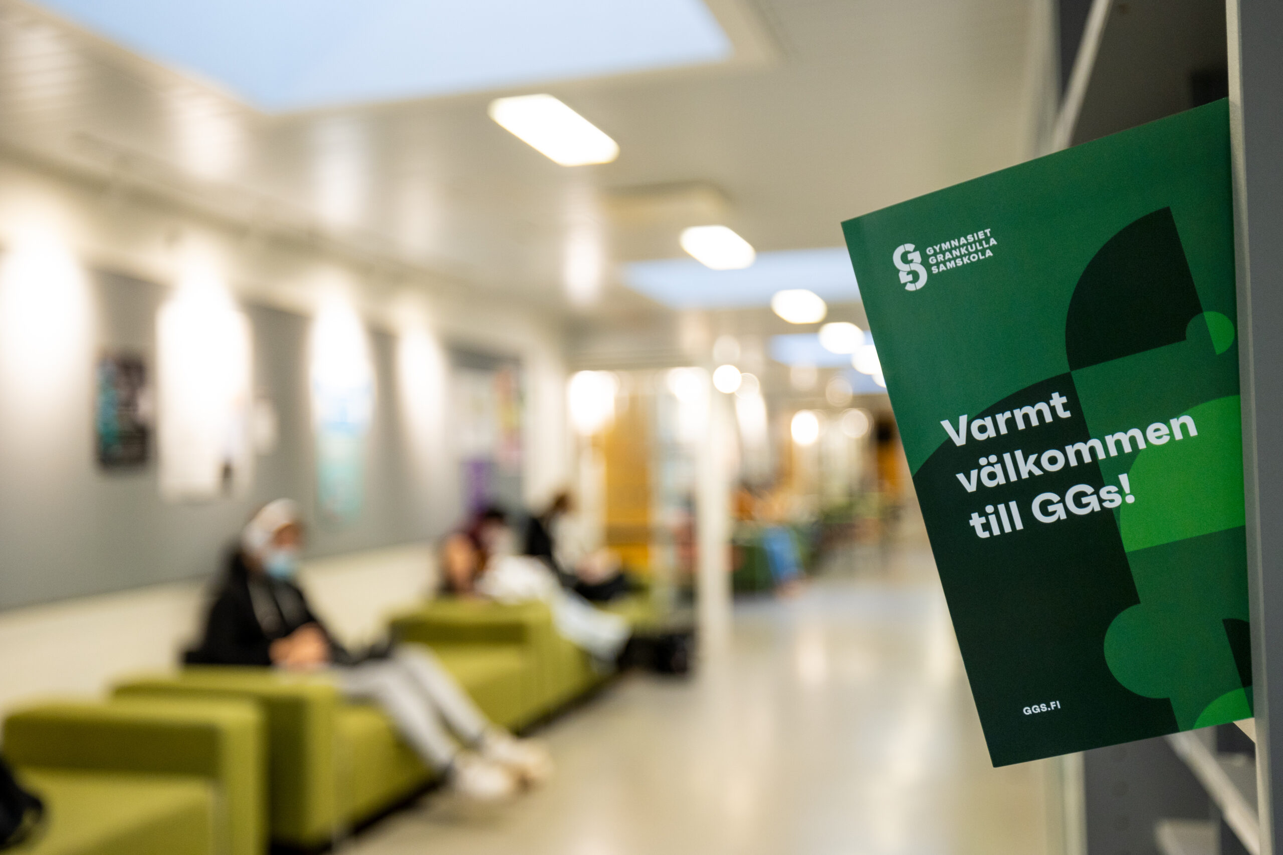 FLyer med txten "Varmt välkommen till Ggs" med skolans korridor i bakgrunden.